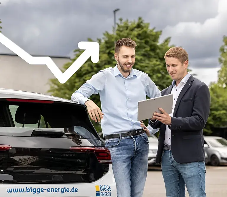 Zwei Mitarbeiter der BIGGE Energie stehen neben einem Firmenwagen. Der eine Mitarbeiter zeigt dem anderen Mitarbeiter Daten und Informationen auf seinem Tablet. 