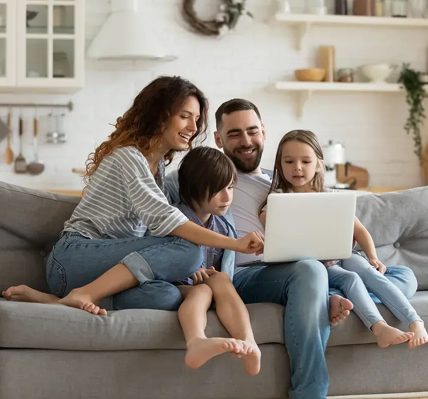 	Eine Familie, Ein Vater, eine Mutter und zwei Kinder sitzen auf dem Sofa und gucken zusammen auf den Laptop. 