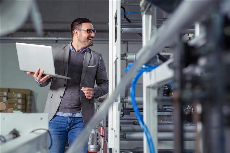 Führungskraft mit Laptop neben einer technischen Anlage.